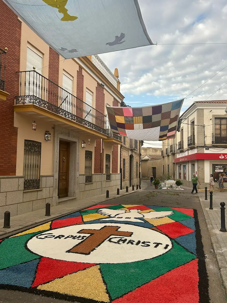 Alfombra decorada para el Corpus Christi 2025 en Los Navalmorales con cruz central, paloma y mosaico de colores vibrantes