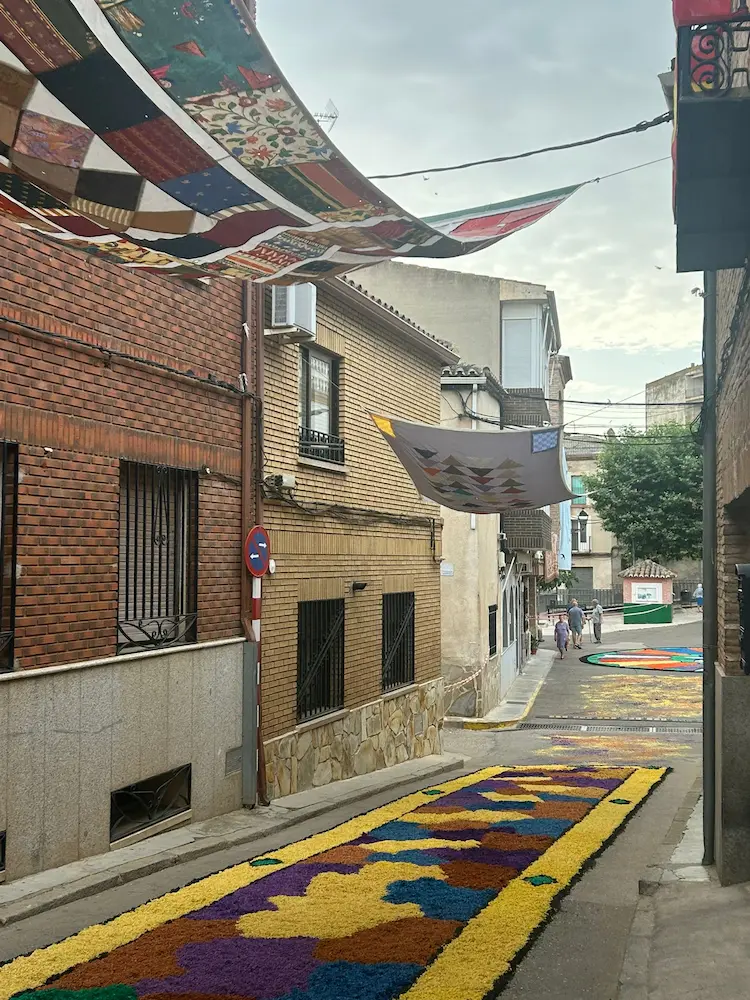 Alfombra multicolor en la calle feria durante el Corpus Christi 2025 en Los Navalmorales, bajo los tradicionales toldos de retales