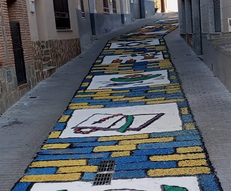 Calle estrecha decorada con alfombra azul y amarilla en el Corpus de Los Navalmorales