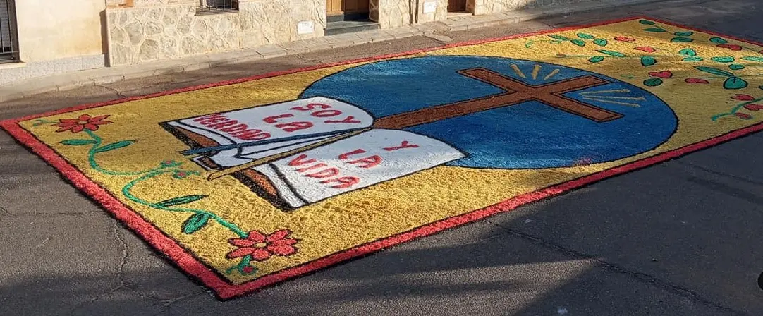 Alfombra de serrín con cruz, cáliz y mensaje religioso durante el Corpus en Los Navalmorales