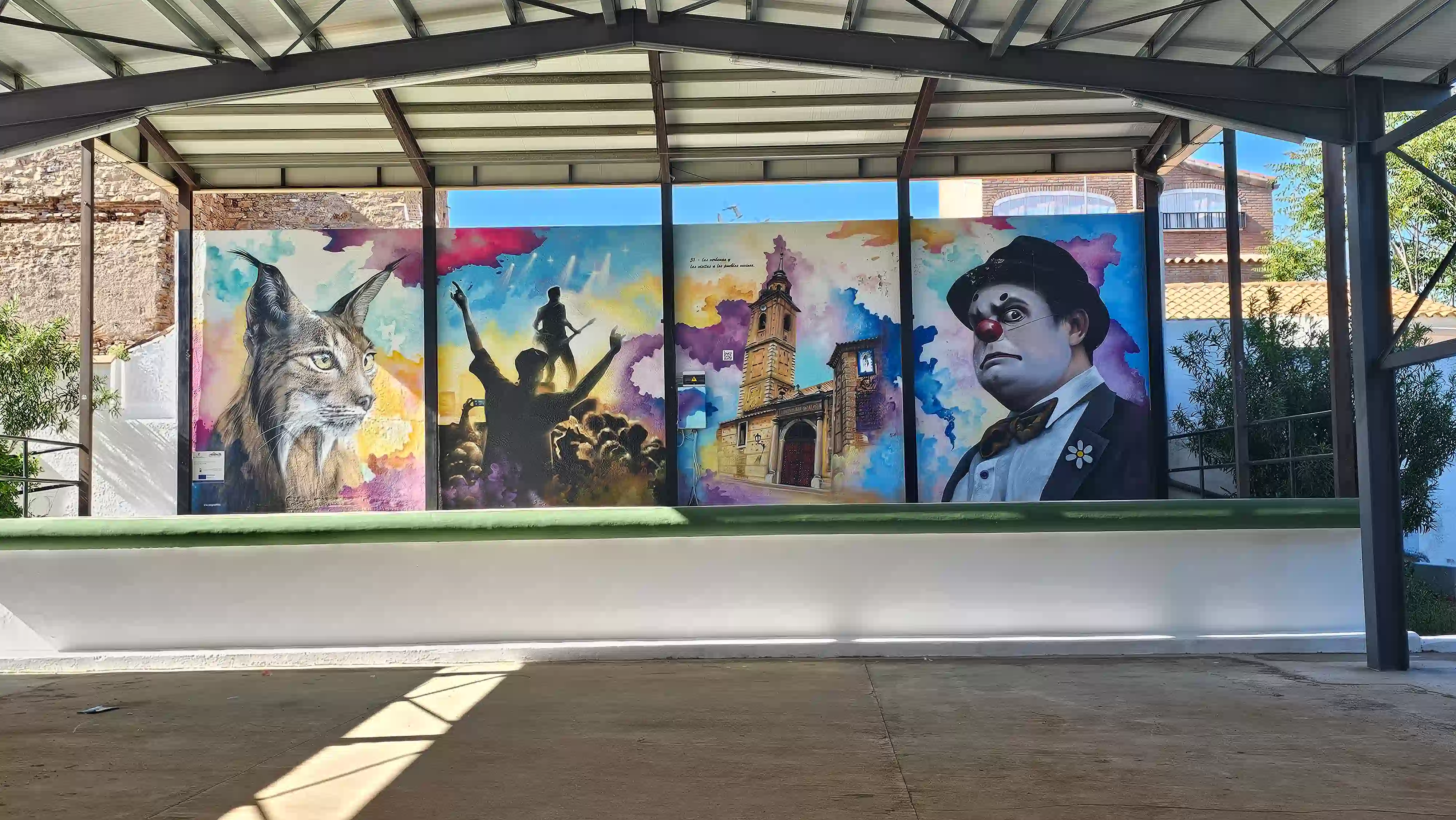 Mural artístico del auditorio al aire libre en el parque de Los Navalmorales con un lince ibérico, músicos, la torre de la iglesia y un payaso